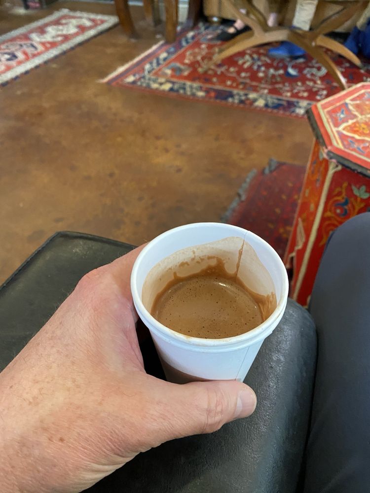 A hand holding a small cup of espresso over a leather lounge chair