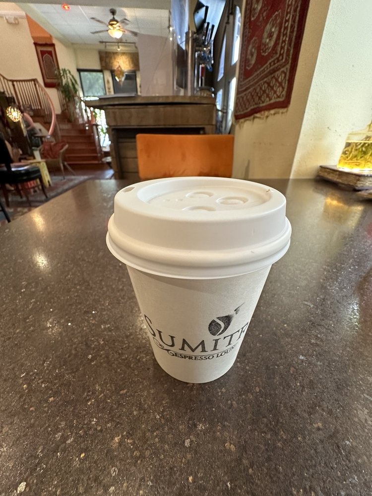 A SumitrA to-go cup on a polished concrete table, rugs and lounge chairs behind