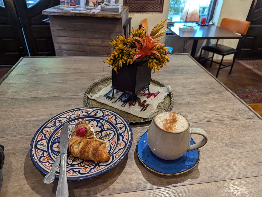 A croissant and a latte on Moroccan plates under a vase of tropical flowers