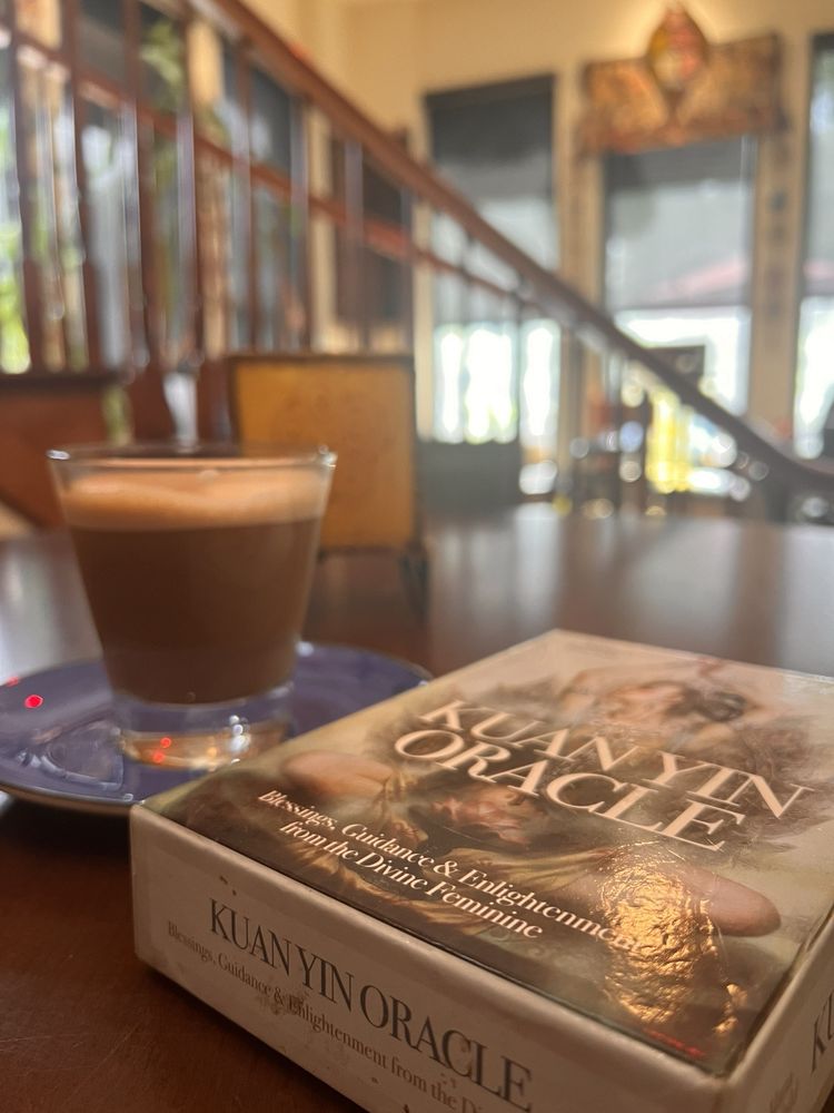 A cortado beside a Kuan Yin Oracle deck on a lounge table