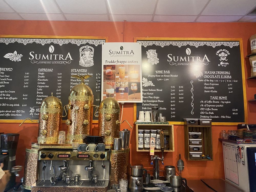 SumitrA's wine bar and drinking chocolate board on the orange wall behind the brass espresso urns