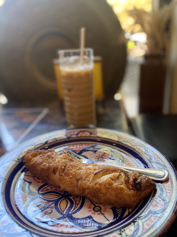 A flaky pastry on a painted Moroccan plate with an iced coffee behind