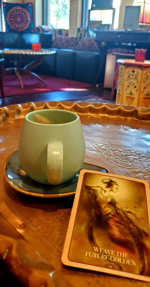 A green mug and an oracle card on a hammered brass table