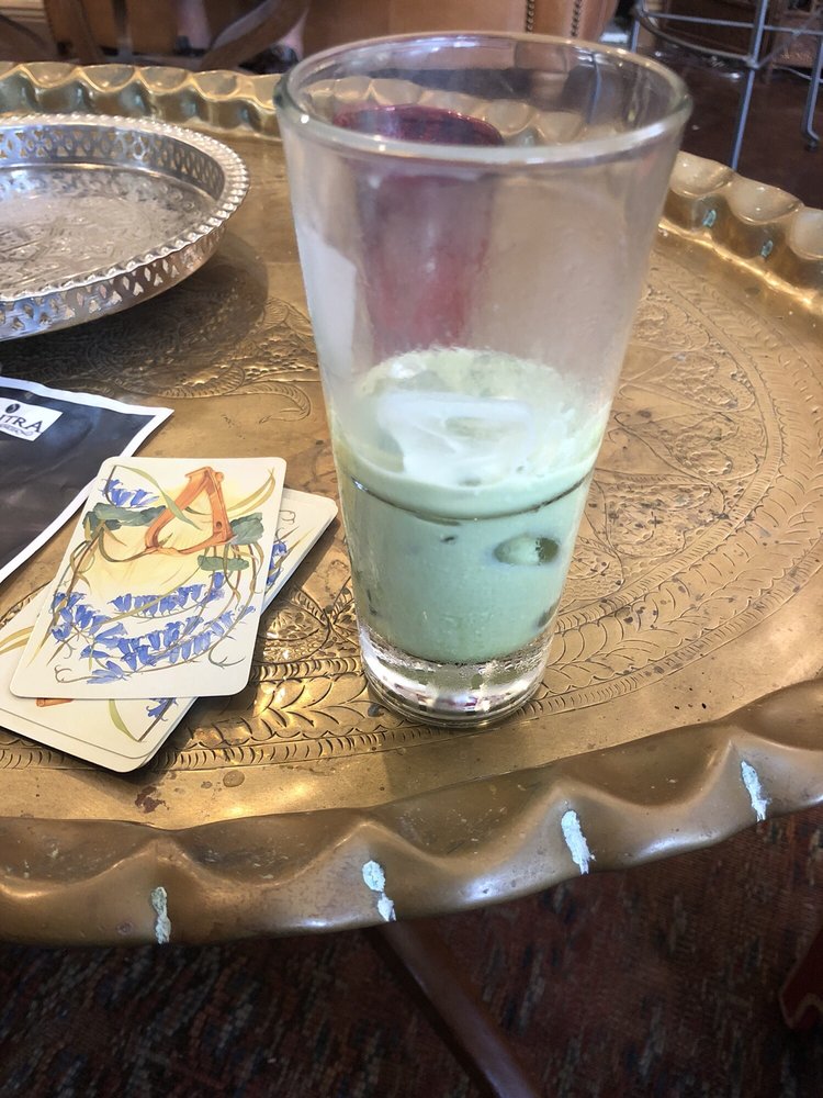 An iced green tonic in a tall glass on a brass tray with a painted card