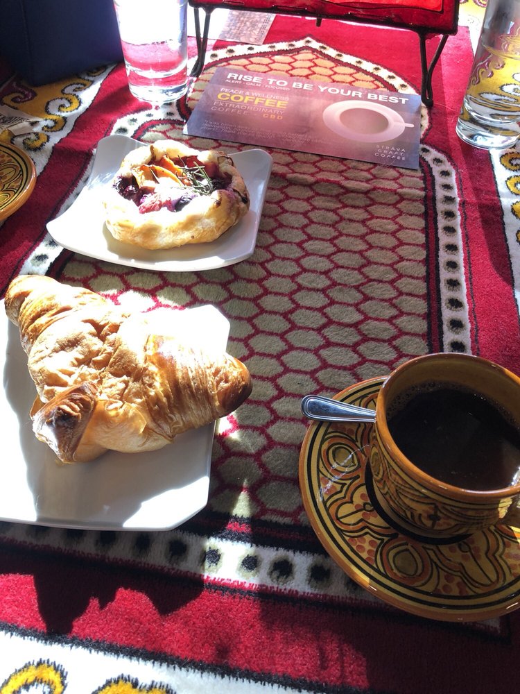 A croissant, a berry galette and a black coffee on a red patterned table runner