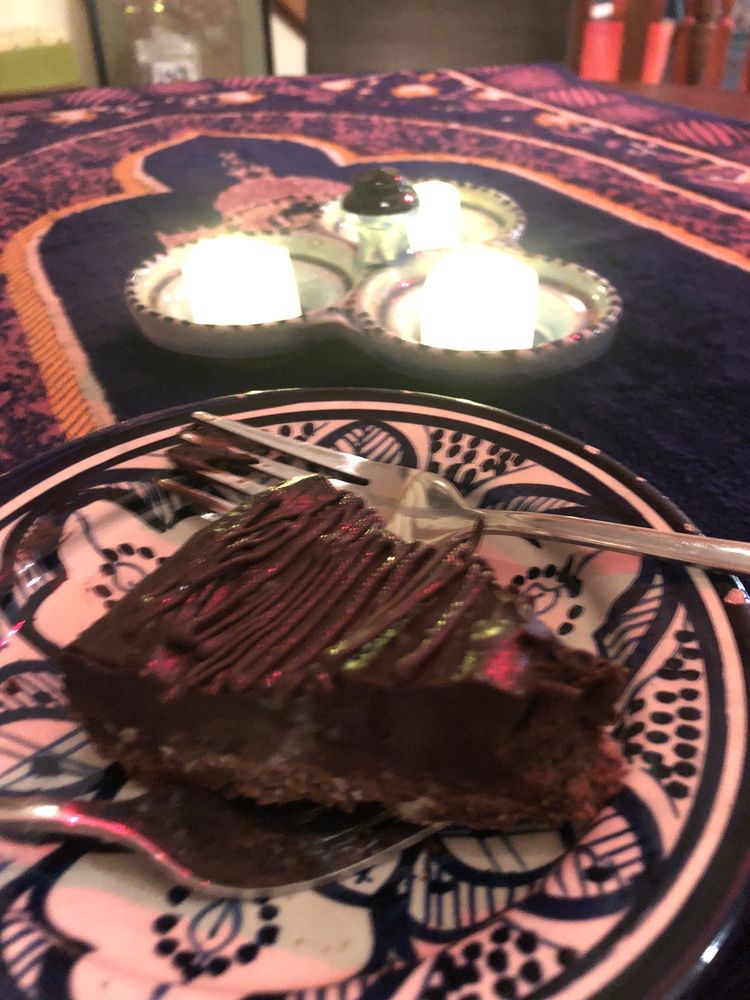 A slice of chocolate tart on a painted Moroccan plate with candles behind