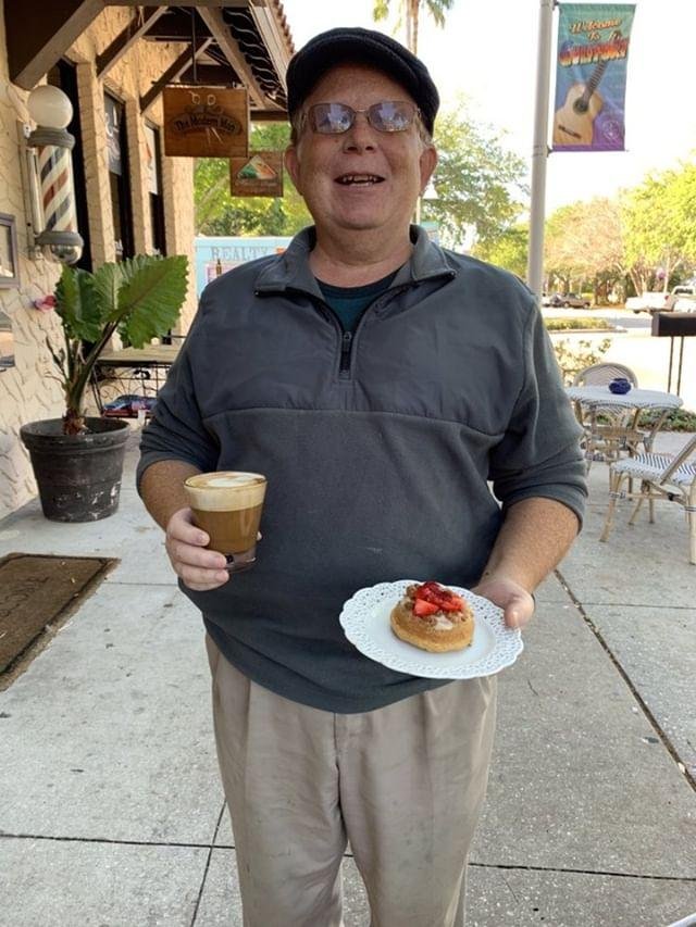 A smiling regular on the sidewalk holding a coffee and a fruit tart