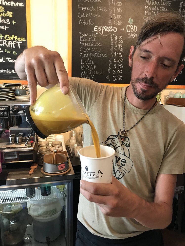 A SumitrA barista pouring a golden latte into a branded cup at the counter