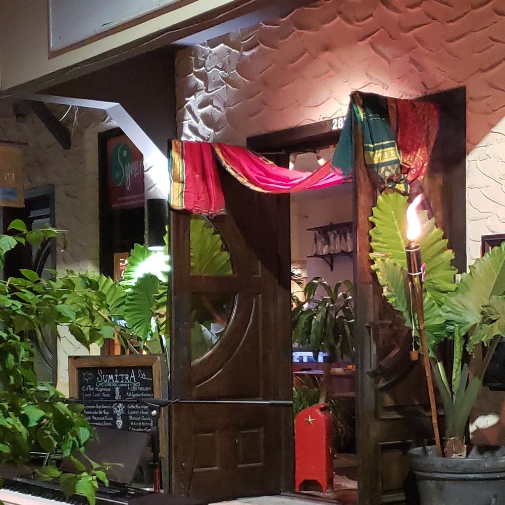SumitrA's carved door draped in red and pink fabric, tall leaves either side