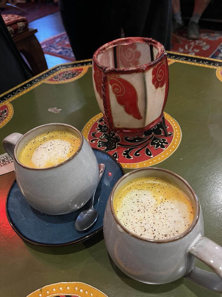 Two golden lattes on a painted green table